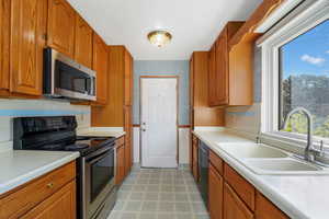 Kitchen with appliances with stainless steel finishes, brown cabinetry, tasteful backsplash, light countertops, and light flooring