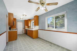 Kitchen with light countertops, wallpapered walls, brown cabinetry, dishwasher, and range