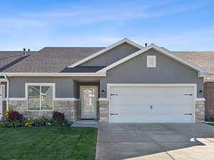 View of front facade featuring stone siding, stucco siding, roof with shingles, and a garage