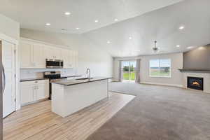 Kitchen featuring vaulted ceiling, open floor plan, stainless steel appliances, an island with sink, and white cabinets