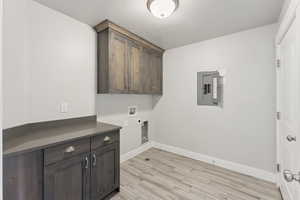 Washroom featuring cabinet space, a textured ceiling, electric panel, light wood-type flooring, and washer hookup