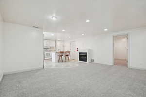 Unfurnished living room featuring light carpet, a fireplace, recessed lighting, a textured ceiling, and crown molding