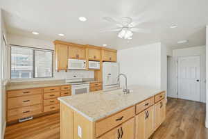 Kitchen with light brown cabinets, white appliances, light wood-style flooring, light stone countertops, and recessed lighting