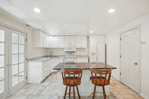 Kitchen featuring a breakfast bar area, white cabinets, white appliances, a center island, and french doors