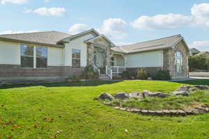 Single story home featuring stucco siding, stone siding, a front yard, and brick siding