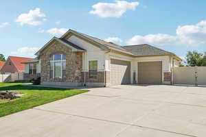 View of front of property with a gate, concrete driveway, stone siding, an attached garage, and a shingled roof