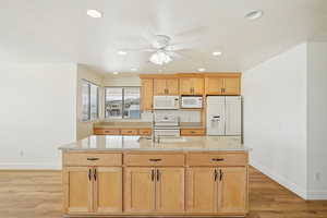 Kitchen with light brown cabinets, light stone counters, white appliances, recessed lighting, and light wood-style flooring