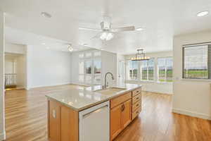 Kitchen with dishwasher, light wood-style floors, light stone counters, open floor plan, and a center island with sink