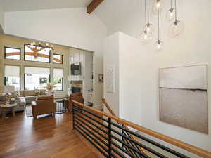 Corridor featuring a chandelier, high vaulted ceiling, wood finished floors, beam ceiling, and an upstairs landing