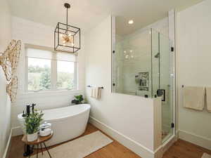 Full bathroom featuring wood finished floors, a soaking tub, a stall shower, recessed lighting, and a chandelier