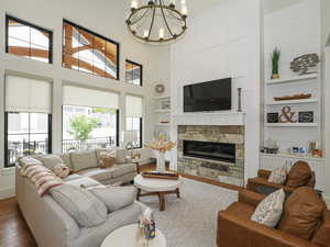 Living area with hardwood / wood-style floors, built in shelves, a stone fireplace, a chandelier, and a towering ceiling