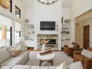 Living area with a towering ceiling, wood finished floors, a stone fireplace, and built in features