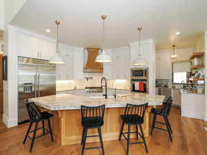 Kitchen with built in appliances, decorative backsplash, a breakfast bar, light wood-style flooring, and premium range hood