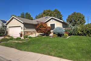 Ranch-style home featuring stucco siding, a front yard, an attached garage, and stone siding