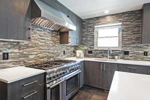 Kitchen with range with two ovens, range hood, tasteful backsplash, dark brown cabinets, and dark stone finish flooring