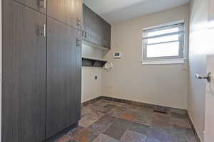 Laundry area with cabinet space, hookup for an electric dryer, and stone tile flooring