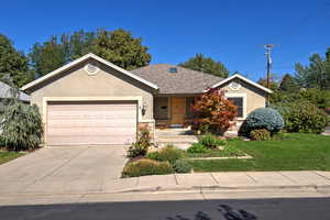 Ranch-style home featuring stone siding, a front lawn, stucco siding, concrete driveway, and a porch