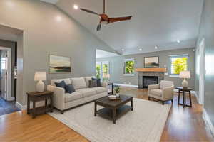 Living area featuring a tiled fireplace, high vaulted ceiling, plenty of natural light, a ceiling fan, and wood finished floors
