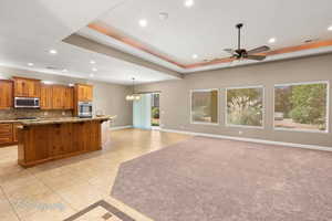 Kitchen with a raised ceiling, recessed lighting, light tile patterned floors, and a kitchen island with sink