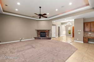 Unfurnished living room with a raised ceiling, a stone fireplace, ceiling fan, light tile patterned floors, and recessed lighting