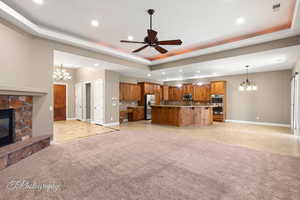 Unfurnished living room featuring a chandelier, a raised ceiling, a stone fireplace, a ceiling fan, and recessed lighting