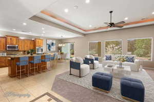 Living room with a raised ceiling, recessed lighting, light tile patterned floors, a chandelier, and a ceiling fan