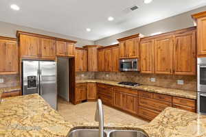 Kitchen featuring brown cabinets, decorative backsplash, light stone countertops, and recessed lighting