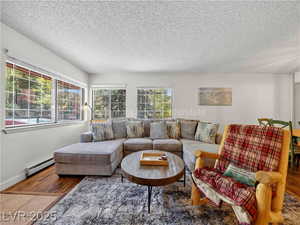 Living room with wood finished floors, a textured ceiling, and a baseboard heating unit