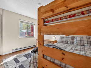 Bedroom featuring wood finished floors, a baseboard radiator, and a textured ceiling