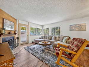 Living room with a fireplace with flush hearth, a textured ceiling, and wood finished floors