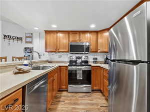 Kitchen with appliances with stainless steel finishes, brown cabinets, light wood-style floors, recessed lighting, and a kitchen bar