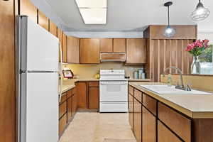 Kitchen with white appliances, decorative light fixtures, brown cabinets, light countertops, and extractor fan