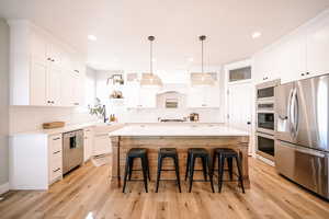 Kitchen with open shelves, appliances with stainless steel finishes, white cabinetry, decorative light fixtures, and a breakfast bar