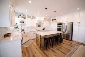 Kitchen featuring open shelves, white cabinetry, appliances with stainless steel finishes, a kitchen bar, and a kitchen island