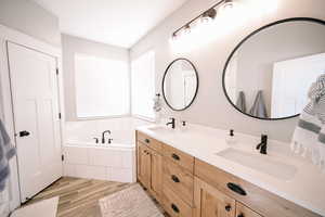 Full bathroom with double vanity, a garden tub, and light wood finished floors