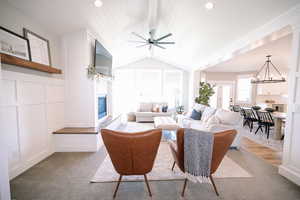 Living area featuring lofted ceiling, a glass covered fireplace, a ceiling fan, a chandelier, and a decorative wall