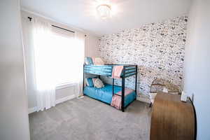 Bedroom with carpet floors, wallpapered walls, and an accent wall