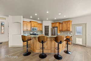 Kitchen featuring light stone countertops, brown cabinetry, a kitchen island, light wood finished floors, and recessed lighting