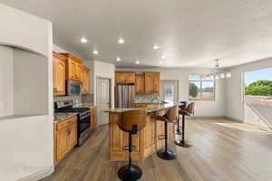 Kitchen featuring light stone counters, stainless steel appliances, a breakfast bar area, an island with sink, and backsplash