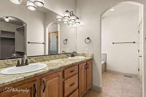 Full bath with double vanity, a stall shower, light tile patterned floors, a garden tub, and a chandelier