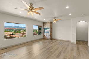 Unfurnished living room with arched walkways, light wood-style flooring, a textured ceiling, recessed lighting, and a ceiling fan