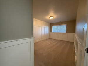 Unfurnished room featuring a decorative wall, wainscoting, and light carpet