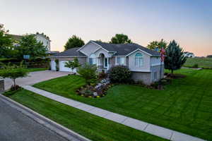 Ranch-style home featuring a front yard, driveway, brick siding, an attached garage, and stucco siding