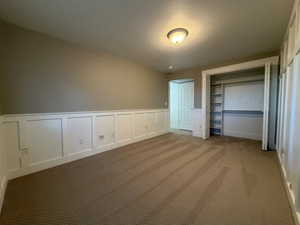 Unfurnished bedroom with a decorative wall, carpet, a wainscoted wall, and a closet