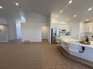 Kitchen featuring arched walkways, white cabinetry, decorative backsplash, stainless steel fridge, and light stone countertops