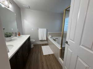 Full bathroom featuring dark wood-style flooring, a bath, a double vanity, and a large shower stall