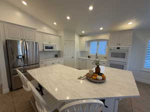 Kitchen featuring white appliances, light tile patterned floors, a breakfast bar area, recessed lighting, and lofted ceiling