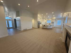 Great Room featuring light tile-patterned floors, arched walkways, recessed lighting, high vaulted ceiling, and light colored carpet