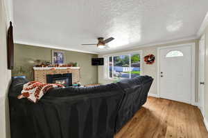 Living room featuring light wood-style floors, ornamental molding, a fireplace, a textured ceiling, and ceiling fan