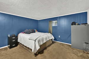 Carpeted bedroom featuring crown molding, wood walls, and a textured ceiling